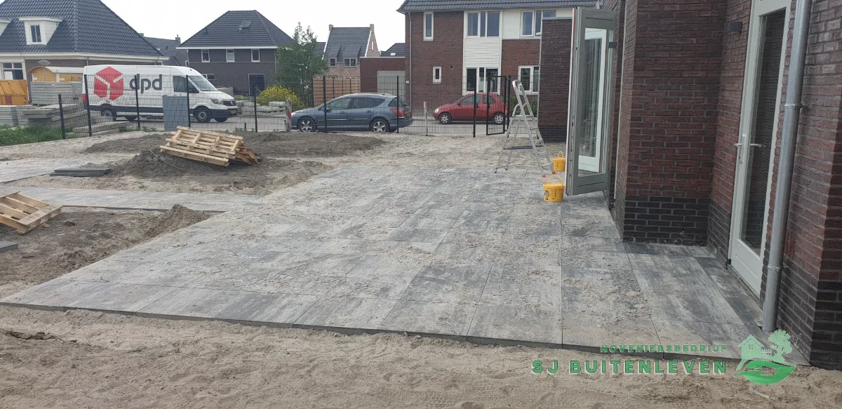 Tuinaanleg in Spanbroek: nieuw terras met grote grijs-zwarte houtlook tegels net gelegd, tuin nog in aanleg.
